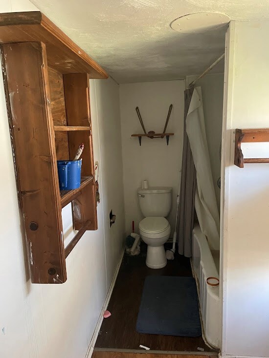 bathroom with wood-type flooring, shower / tub combo, and toilet