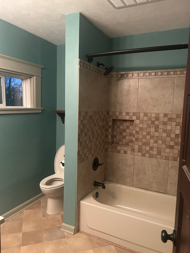 bathroom featuring tiled shower / bath combo, tile patterned floors, a textured ceiling, and toilet