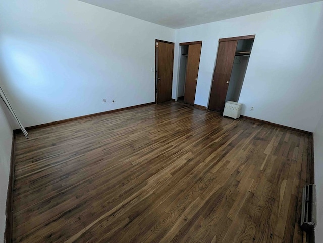 unfurnished bedroom with dark wood-type flooring and two closets