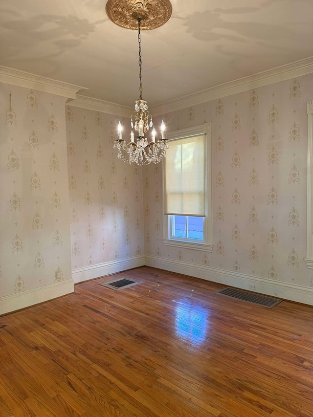 empty room with hardwood / wood-style flooring, ornamental molding, and a chandelier