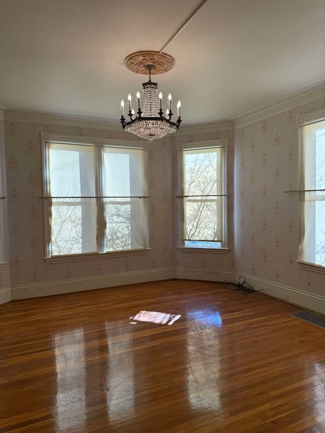 unfurnished room featuring hardwood / wood-style flooring, crown molding, and an inviting chandelier