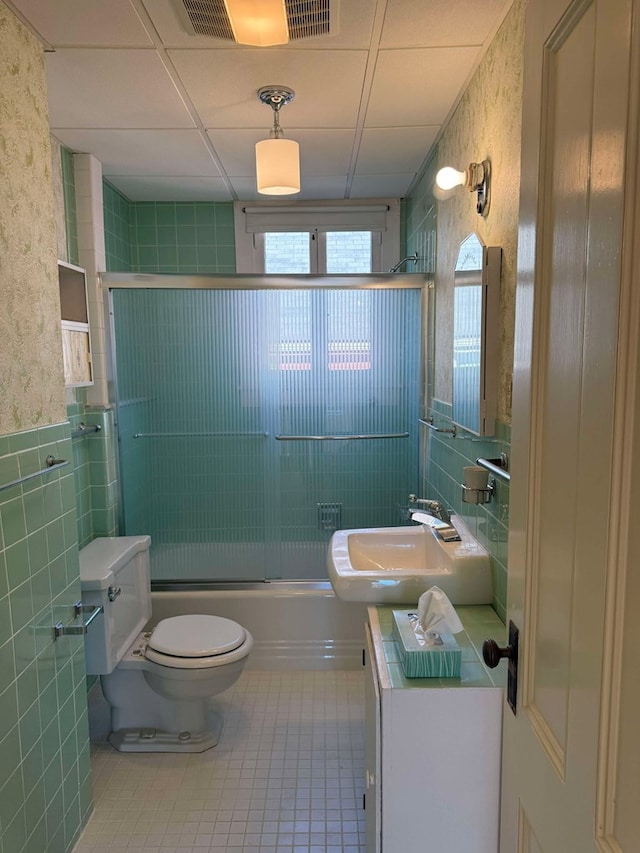 full bathroom featuring sink, a drop ceiling, tile patterned flooring, toilet, and shower / bath combination with glass door