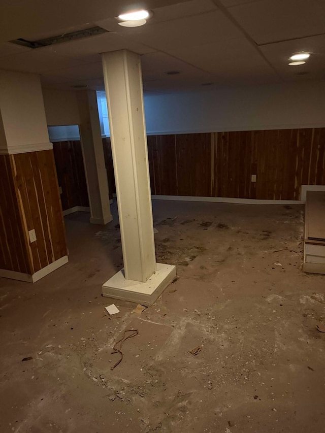 basement with a paneled ceiling and wood walls