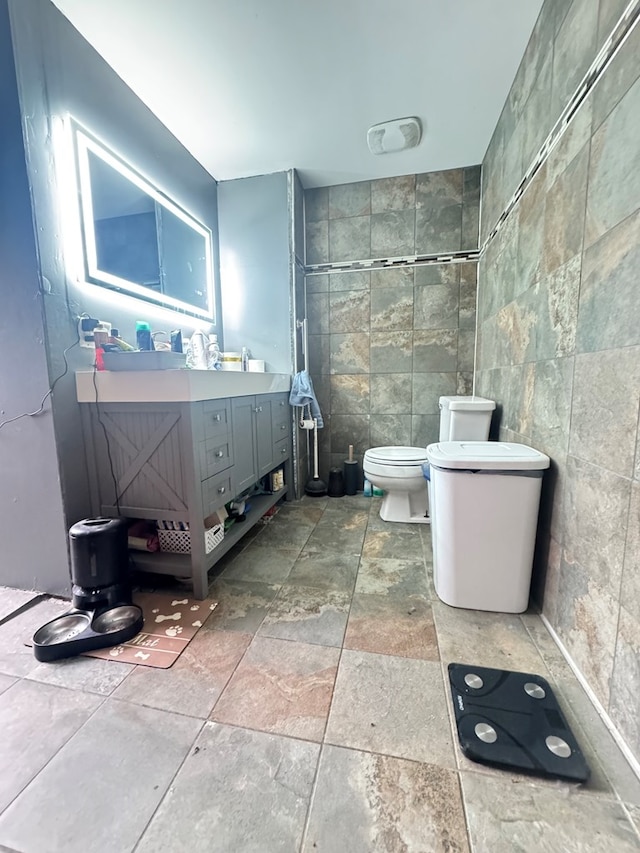 bathroom with vanity, toilet, and tile walls