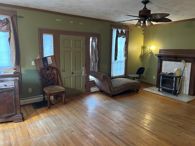 sitting room featuring a baseboard heating unit, light wood-type flooring, ornamental molding, and a wood stove