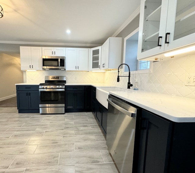 kitchen with sink, light stone counters, ornamental molding, stainless steel appliances, and white cabinets