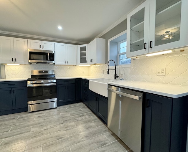 kitchen featuring sink, white cabinetry, stainless steel appliances, light stone counters, and ornamental molding