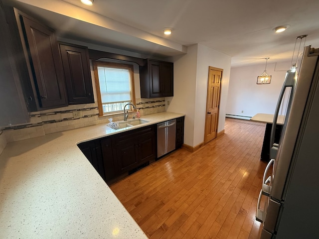 kitchen with sink, a baseboard radiator, stainless steel appliances, backsplash, and decorative light fixtures