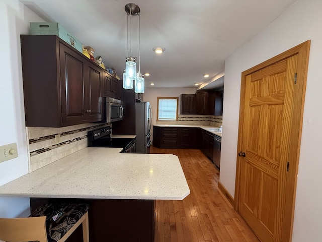 kitchen featuring decorative light fixtures, kitchen peninsula, stainless steel appliances, and tasteful backsplash