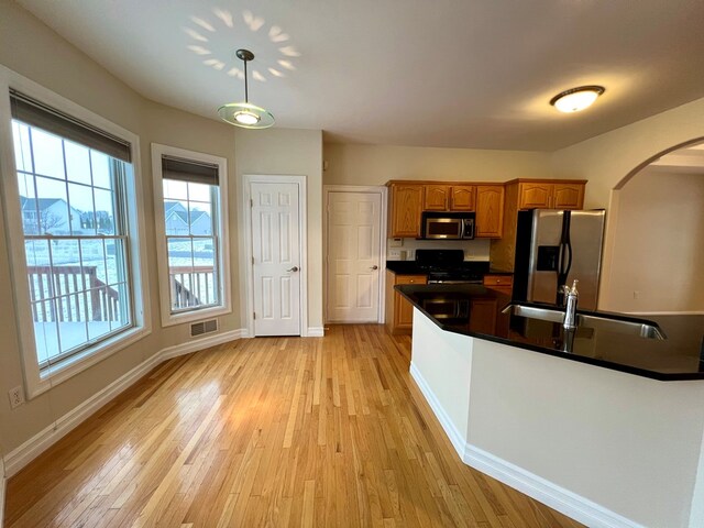 kitchen with appliances with stainless steel finishes, sink, pendant lighting, and light wood-type flooring