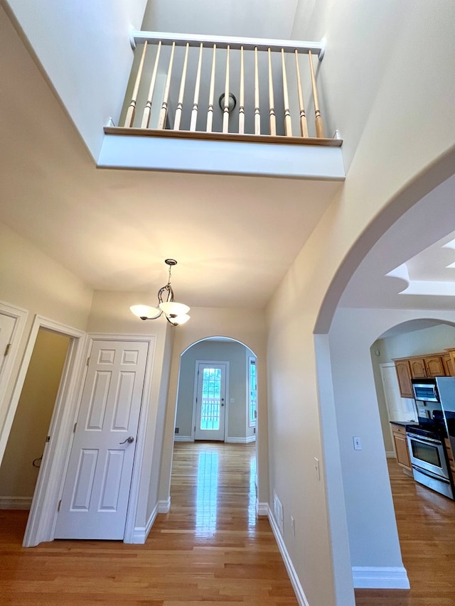 hall with a high ceiling, a notable chandelier, and light wood-type flooring