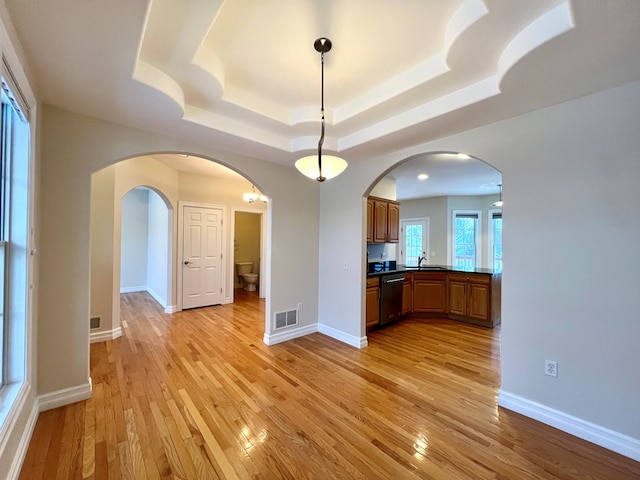 kitchen with sink, light hardwood / wood-style flooring, hanging light fixtures, stainless steel dishwasher, and a raised ceiling