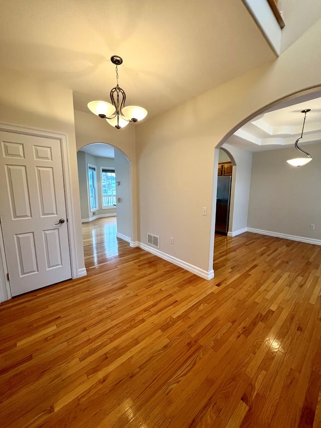 empty room with a tray ceiling, a notable chandelier, and hardwood / wood-style flooring