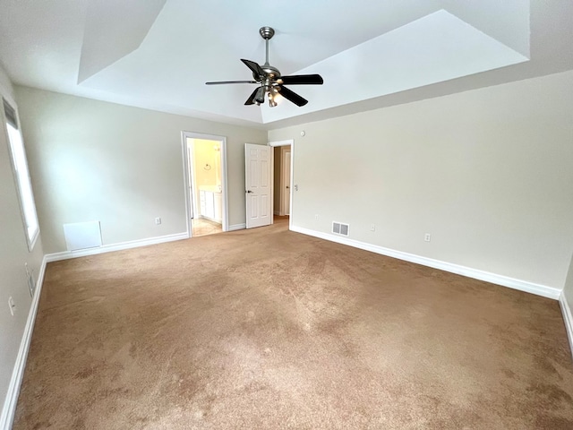 unfurnished bedroom featuring ceiling fan, ensuite bath, a tray ceiling, and carpet