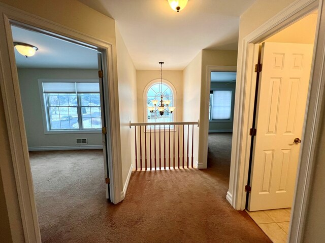 hallway with light carpet and a notable chandelier