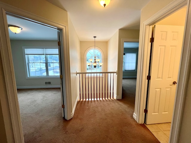 hallway with light colored carpet and a notable chandelier