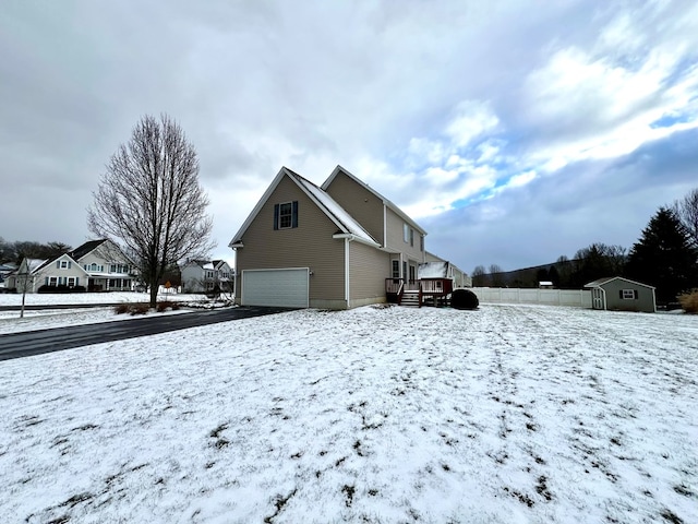 snow covered property featuring a wooden deck, a storage shed, and a garage