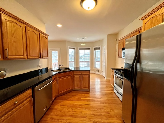 kitchen with appliances with stainless steel finishes, kitchen peninsula, sink, and light wood-type flooring