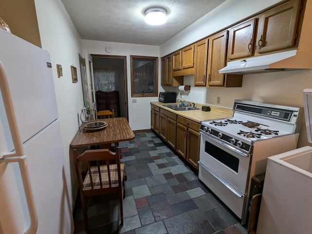 kitchen featuring gas stove, sink, white fridge, and a textured ceiling