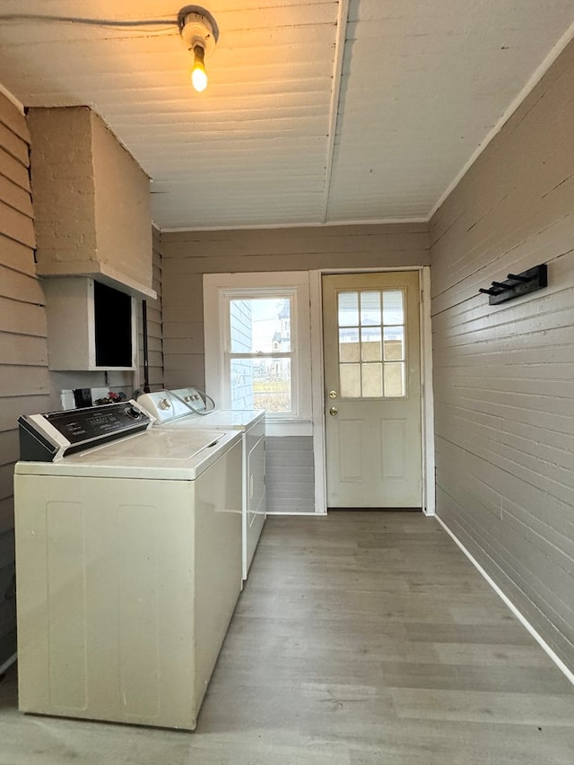 washroom with separate washer and dryer, wooden walls, and light hardwood / wood-style flooring