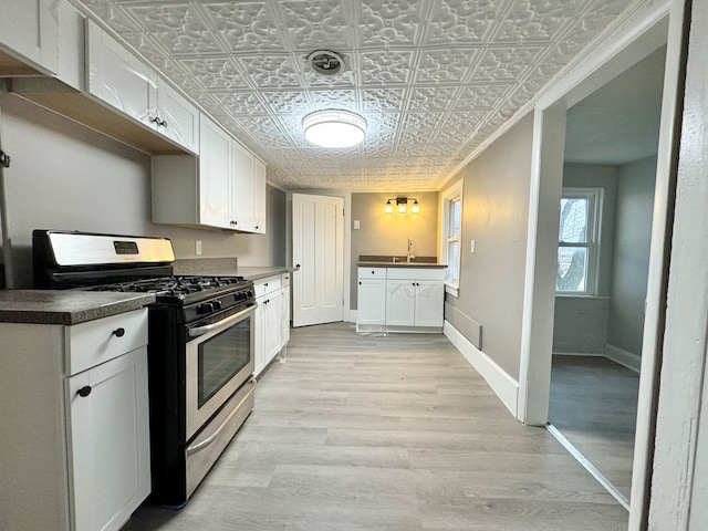 kitchen with white cabinets, stainless steel gas stove, light hardwood / wood-style flooring, and sink