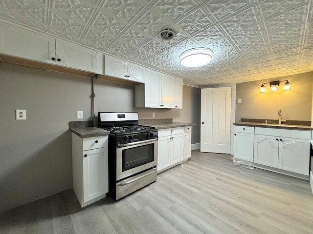 kitchen featuring white cabinets, light wood-type flooring, stainless steel range with gas cooktop, and sink