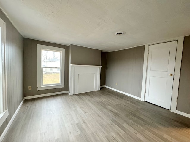 unfurnished living room featuring a textured ceiling, light hardwood / wood-style floors, and wooden walls