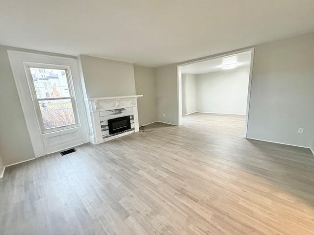 unfurnished living room featuring a high end fireplace and light hardwood / wood-style floors