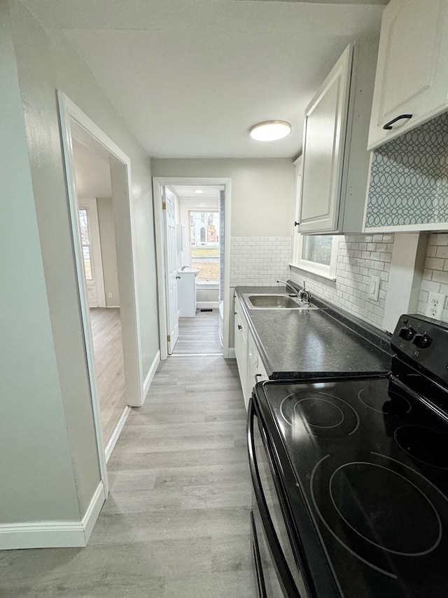 kitchen featuring sink, black electric range, backsplash, light hardwood / wood-style floors, and white cabinets