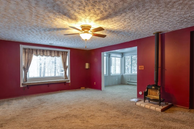 carpeted spare room featuring ceiling fan, baseboard heating, a textured ceiling, and a wood stove