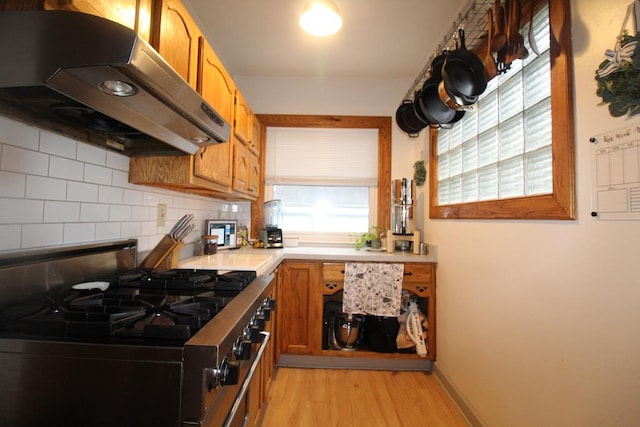 kitchen featuring ventilation hood, stainless steel stove, gas stovetop, light wood-type flooring, and tasteful backsplash