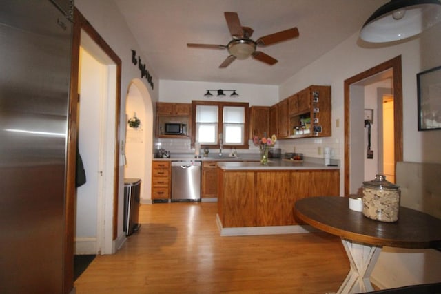 kitchen with backsplash, ceiling fan, light wood-type flooring, appliances with stainless steel finishes, and kitchen peninsula