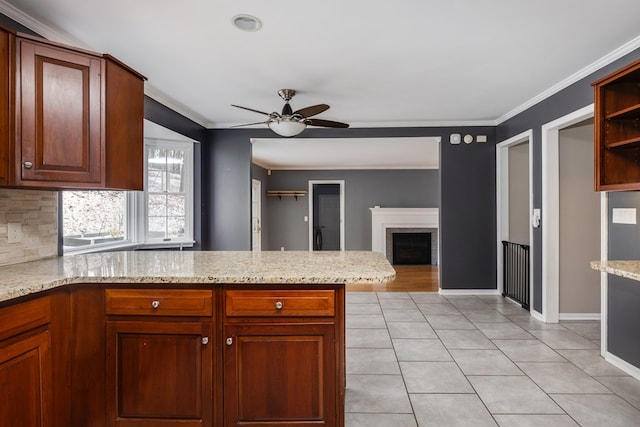 kitchen with light tile patterned floors, ornamental molding, ceiling fan, light stone countertops, and backsplash