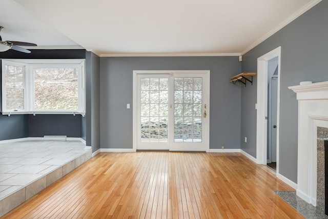 unfurnished living room featuring a tiled fireplace, ornamental molding, ceiling fan, and light wood-type flooring