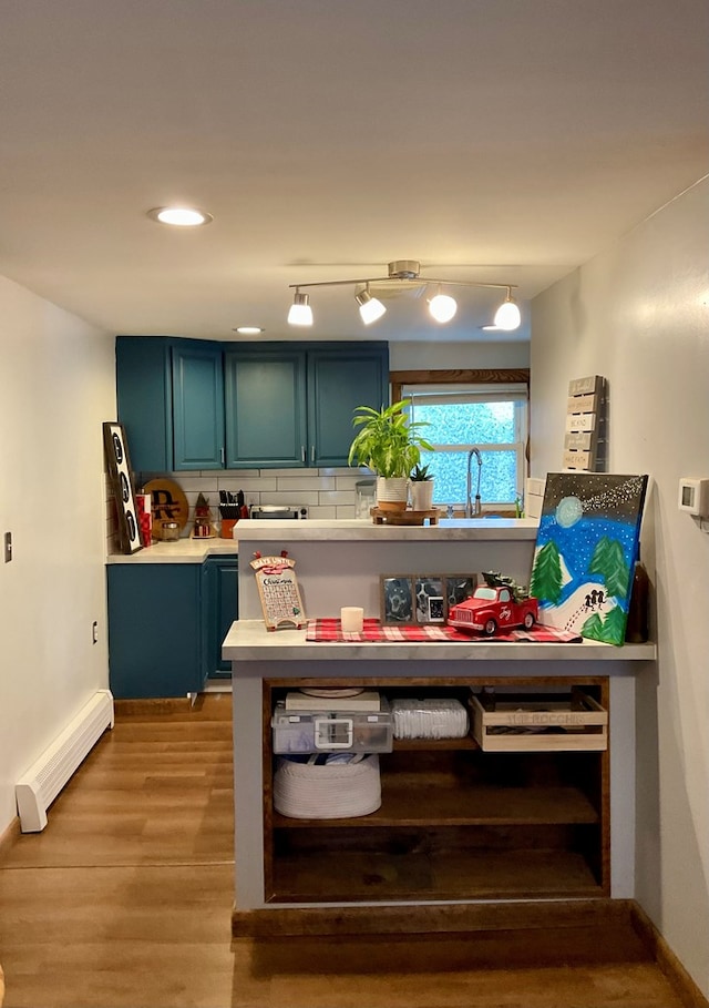 kitchen with light wood-type flooring, blue cabinetry, a baseboard heating unit, backsplash, and sink