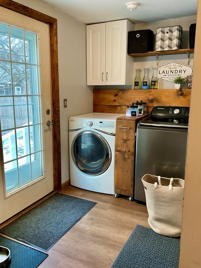 clothes washing area with cabinets, washing machine and clothes dryer, plenty of natural light, and light hardwood / wood-style flooring