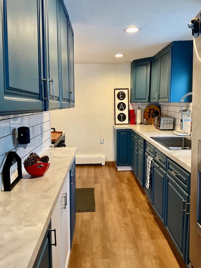 kitchen with baseboard heating, light hardwood / wood-style flooring, blue cabinets, and decorative backsplash