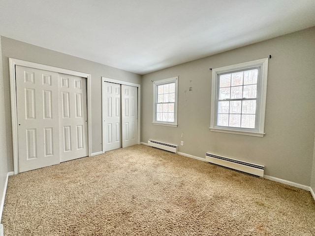 unfurnished bedroom with light colored carpet, baseboard heating, and multiple closets