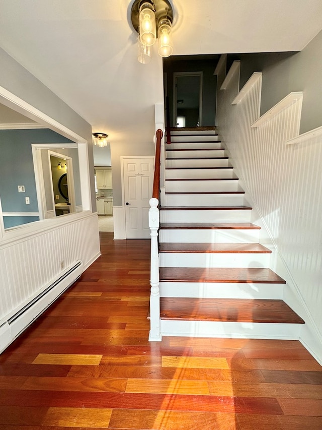 stairs featuring baseboard heating, ornamental molding, and wood-type flooring