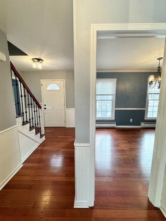 foyer entrance featuring dark wood-type flooring, baseboard heating, a chandelier, and crown molding