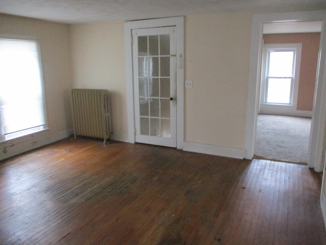 empty room featuring radiator, dark wood-type flooring, and a healthy amount of sunlight