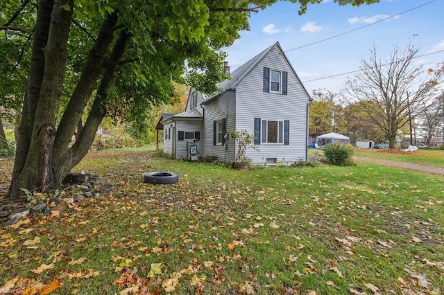 view of side of property featuring an outdoor fire pit, a chimney, and a lawn