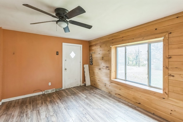 foyer entrance with wood walls, wood finished floors, visible vents, baseboards, and a ceiling fan