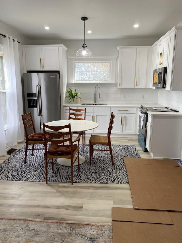 kitchen featuring sink, stainless steel appliances, light hardwood / wood-style floors, decorative light fixtures, and white cabinets