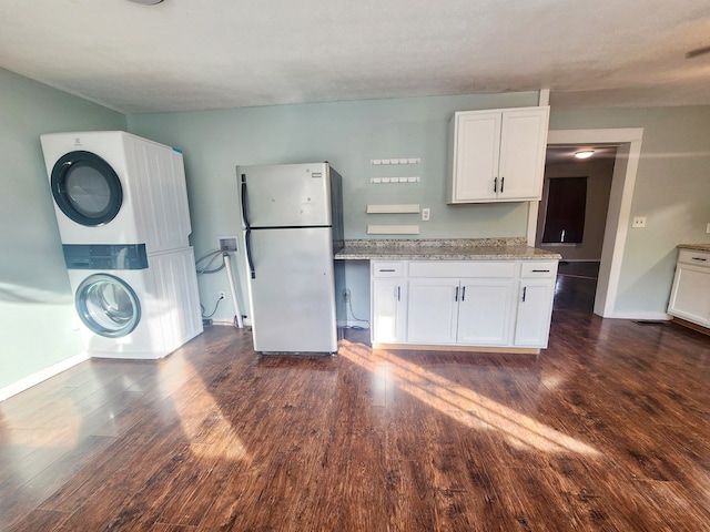 kitchen with stacked washer and dryer, stainless steel refrigerator, white cabinetry, light stone countertops, and dark hardwood / wood-style flooring