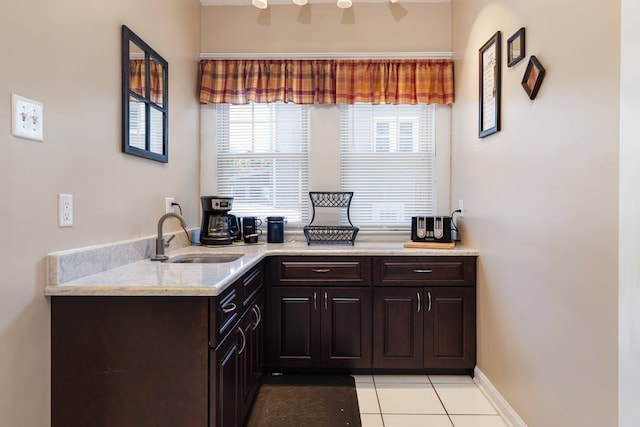 kitchen with sink, light tile patterned flooring, dark brown cabinets, and light stone countertops