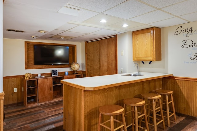 bar featuring sink, dark hardwood / wood-style flooring, wood walls, and a drop ceiling