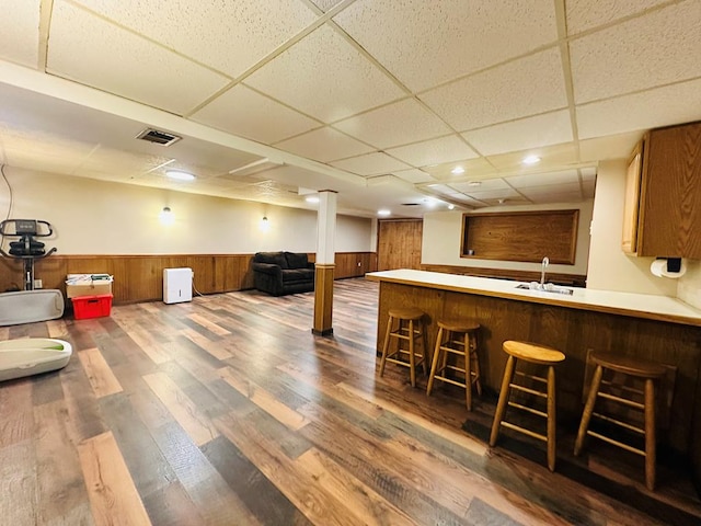 bar with sink, a paneled ceiling, wooden walls, and hardwood / wood-style flooring