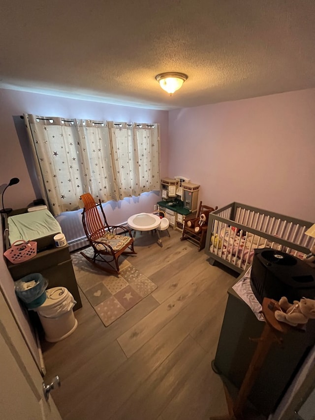 bedroom featuring a nursery area, a textured ceiling, and hardwood / wood-style flooring