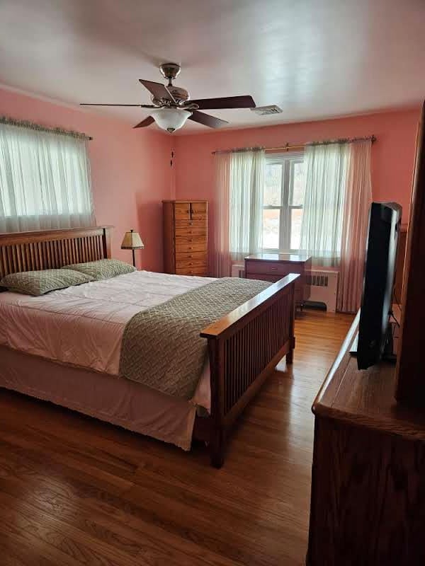 bedroom with ceiling fan, wood-type flooring, and radiator heating unit